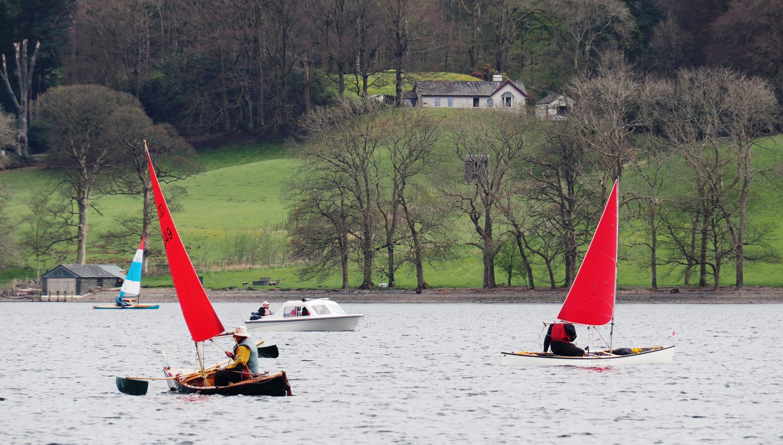3 canoes racing under sail on Coniston Water, with a small hire launch pottering about as well