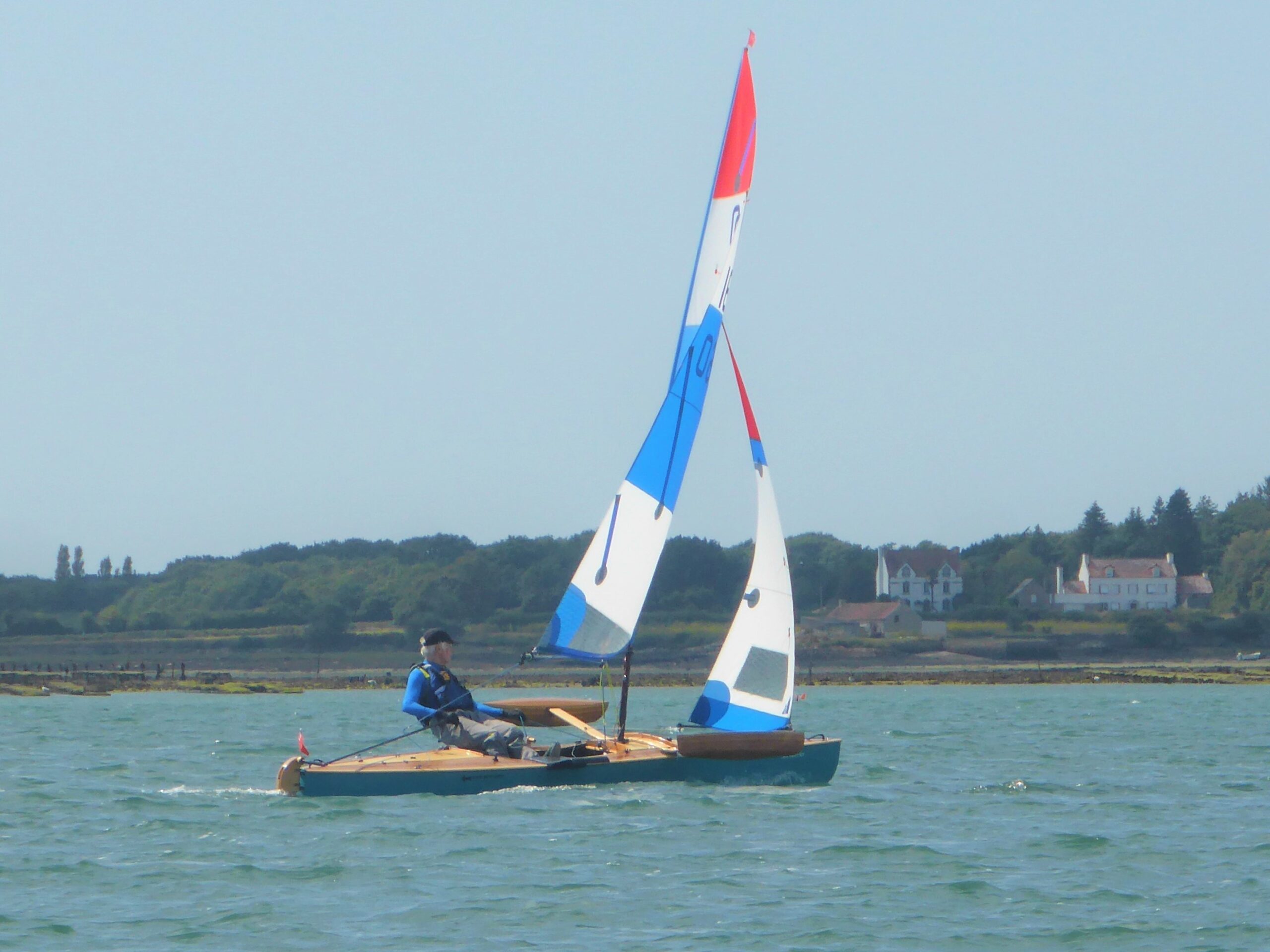 Decked sailing canoe with red, white and blue sails