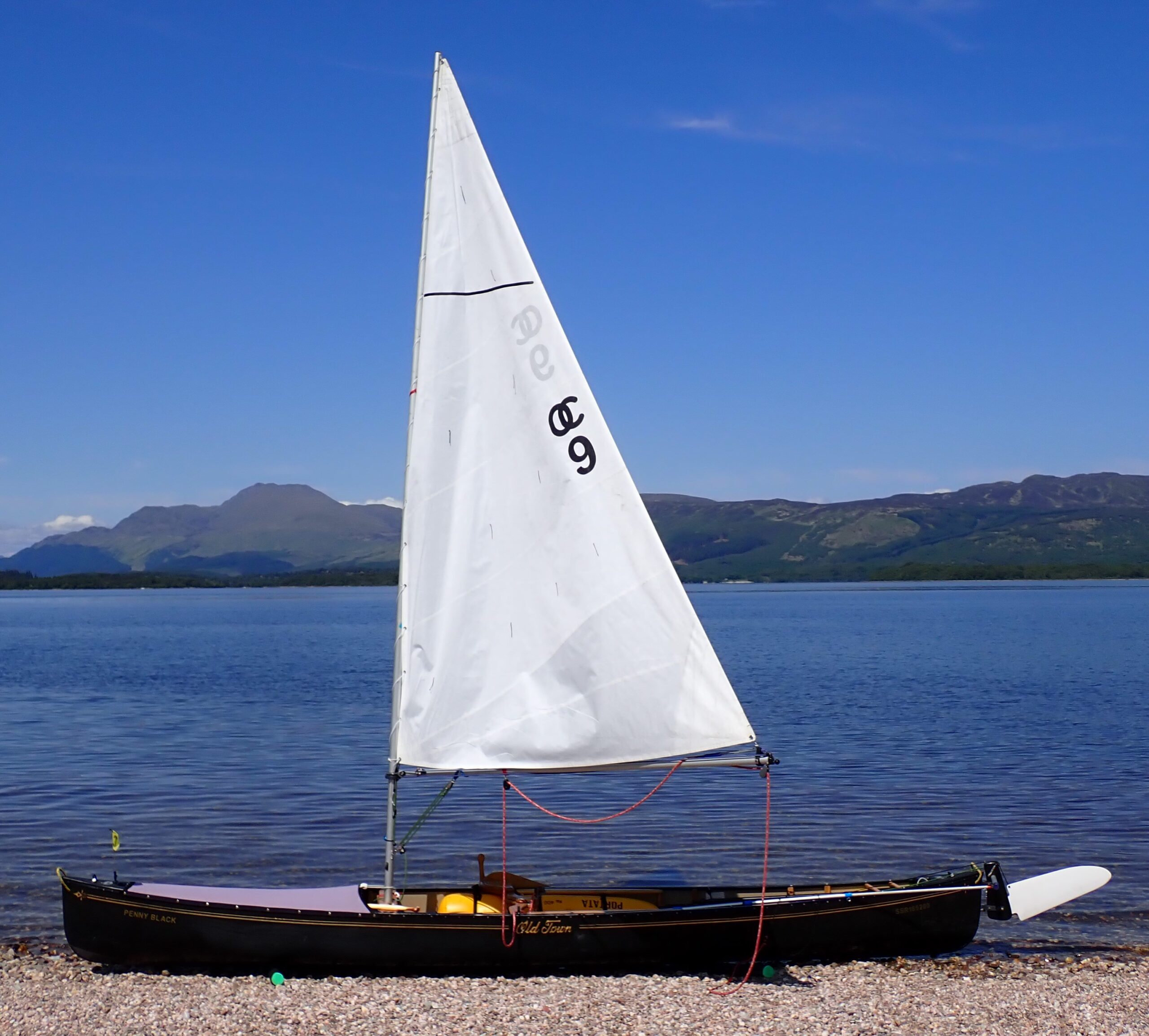 black sailing canoe on stony beach with a loch and mountain background
